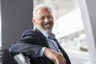 Portrait of smiling mature businessman sitting in waiting area - DIGF07463