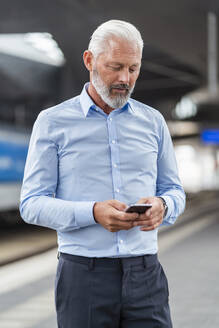 Älterer Geschäftsmann, der am Bahnsteig ein Mobiltelefon benutzt - DIGF07471