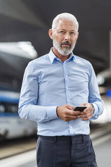 Älterer Geschäftsmann mit Mobiltelefon am Bahnsteig - DIGF07472