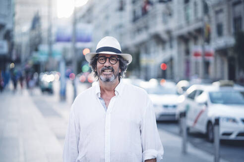 Porträt eines attraktiven älteren Mannes mit weißer Kleidung und Hut, der in einer Straße in Madrid vor der Kamera posiert - OCMF00463