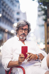 Älterer Mann schreibt eine SMS auf seinem Handy, während er in einem Straßencafé in Madrid sitzt - OCMF00470