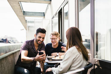 Drei Freunde überprüfen ihr Handy auf der Terrasse eines Hotelzimmers - MASF12790