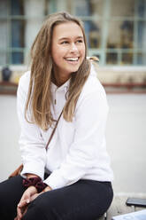 Smiling teenage girl looking away while sitting in schoolyard - MASF12811