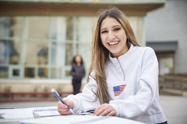 Porträt eines lächelnden Teenagers, der am Tisch auf dem Schulhof sitzt - MASF12817