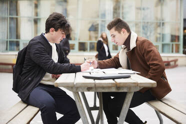 Männliche Freunde im Teenageralter lernen am Tisch auf dem Schulhof - MASF12825