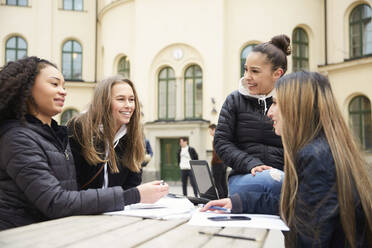 Lächelnde multiethnische Freundinnen beim Lernen am Tisch auf dem Schulhof - MASF12827