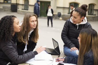 Multiethnische Freundinnen diskutieren beim Lernen am Tisch auf dem Schulhof - MASF12831