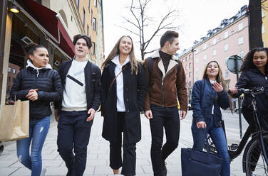 Smiling male and female teenage friends walking on footpath in city - MASF12832