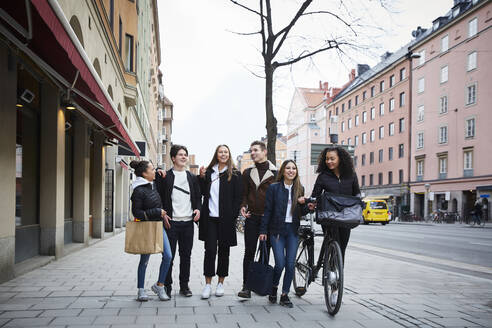 Lächelnde männliche und weibliche Teenager-Freunde gehen auf dem Bürgersteig in der Stadt - MASF12833
