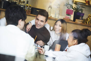 Männliche und weibliche Freunde sitzen lächelnd am Tisch in einem Cafe - MASF12846