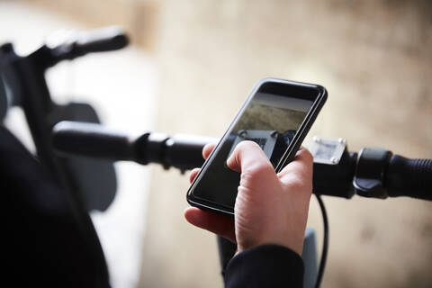 Ausgeschnittenes Bild eines Mädchens, das ein Mobiltelefon über einem elektrischen Roller benutzt, lizenzfreies Stockfoto