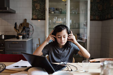 Boy using headphones while doing homework at home - MASF12891