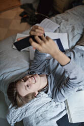 Hohe Winkel Ansicht der lächelnden Teenager mit Handy während des Studiums im Schlafzimmer - MASF12923