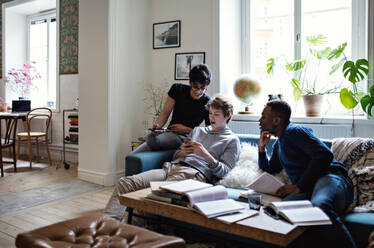 Male friends using mobile phones while sitting on sofa during homework in living room - MASF12935