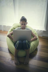 Mixed race girl using laptop in beanbag chair - BLEF09712