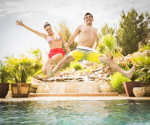 Couple jumping into swimming pool - BLEF09720