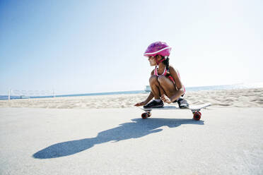 Mixed race girl riding skateboard at beach - BLEF09729