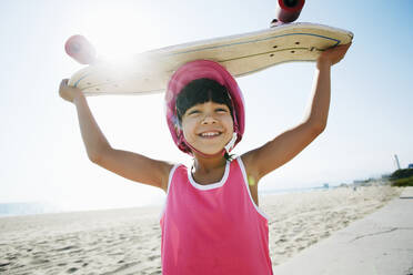 Gemischtrassiges Mädchen hält Skateboard am Strand - BLEF09736