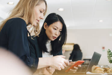 Female colleagues using smart phones while sitting at conference table in board room - MASF12990