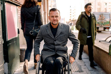 Disabled mature man looking away while sitting on wheelchair in city - MASF13007
