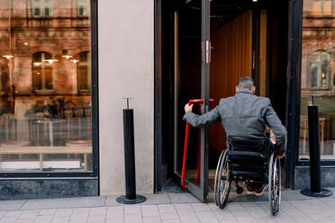 Rear view of disabled mature man sitting on wheelchair while entering in store - MASF13009