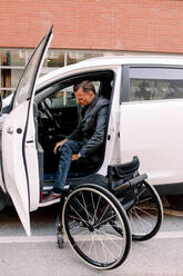 Volle Länge Seitenansicht der reifen behinderten Mann Aussteigen aus dem Auto mit Rollstuhl auf der Straße in der Stadt - MASF13012