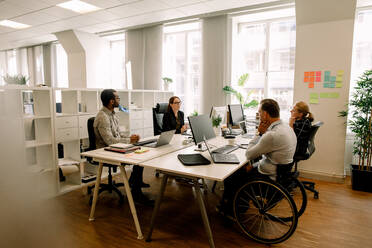 Business colleagues with disabled sales manager working at desk in office - MASF13055