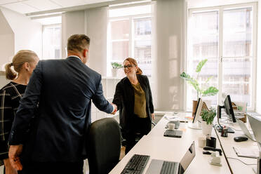 Businesswoman shaking hand with businessman while standing in office - MASF13057