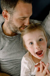 Porträt eines schreienden Mädchens, das mit seinem Vater auf dem Bett im Schlafzimmer liegt - MASF13070