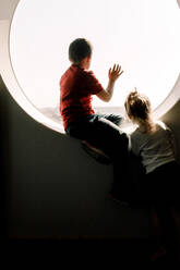 Siblings looking through window from hotel room - MASF13074