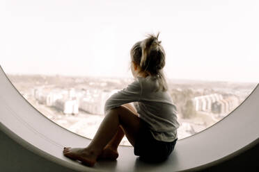 Mädchen in voller Länge auf der Fensterbank eines Hotelzimmers sitzend - MASF13075