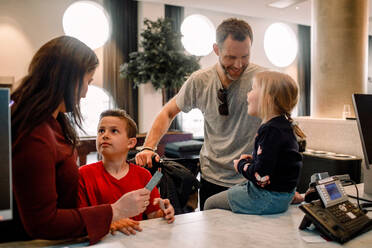 Lächelnde Eltern im Gespräch mit Kindern an der Rezeption im Hotel - MASF13097