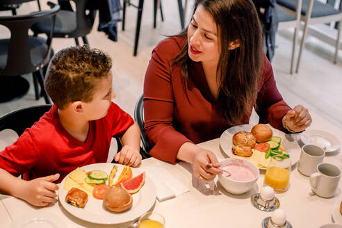 Blick von oben auf die Mutter, die sich mit ihrem Sohn unterhält, während sie beim Frühstück im Restaurant am Tisch sitzt - MASF13105