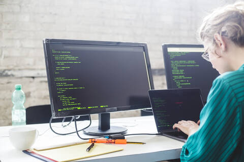 Seitenansicht einer Geschäftsfrau, die an einem Start-up-Projekt arbeitet, während sie im Büro kodiert, lizenzfreies Stockfoto