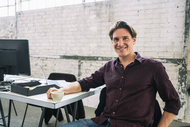 Portrait of confident male IT professional sitting at desk in creative office - MASF13112