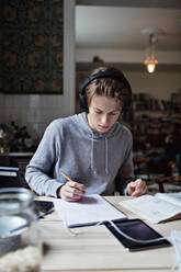 Studierender Teenager hört Musik, während er zu Hause am Tisch lernt - MASF13130