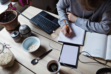 High angle view of teenage boy writing on book while using digital tablet for homework - MASF13142