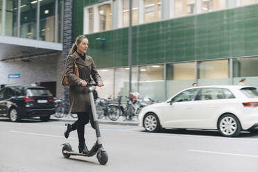 Full length of confident businesswoman riding electric push scooter on street in city - MASF13259