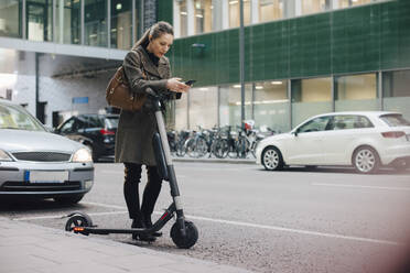 Weiblicher Pendler in voller Länge mit Smartphone am Straßenrand in der Stadt - MASF13261