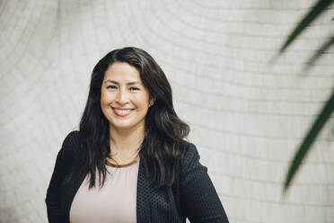 Portrait of smiling businesswoman standing against wall at office - MASF13286