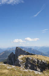 Distant view of hiker standing on Spinnerin peak against blue sky - GWF06149