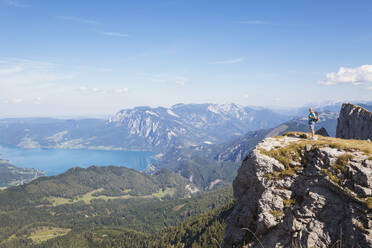 Full length of hiker standing on Spinnerin peak while looking at Attersee against blue sky - GWF06155