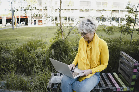 Ältere Frau sitzt auf einer Bank im Freien und benutzt einen Laptop, lizenzfreies Stockfoto