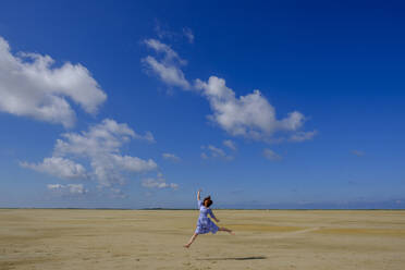 In voller Länge von Teenager-Mädchen springen am Strand gegen blauen Himmel an einem sonnigen Tag - LBF02628