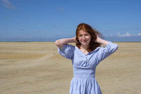 Porträt eines lächelnden Mädchens im blauen Kleid am Strand gegen den Himmel an einem sonnigen Tag, lizenzfreies Stockfoto