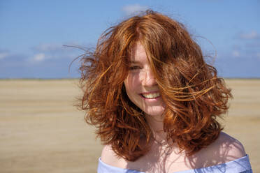 Close-up portrait of carefree redhead teenage girl standing at beach against sky on sunny day - LBF02632