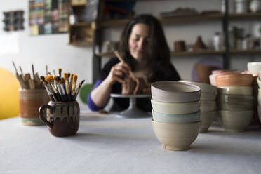 Potter shaping clay in her workshop, focus on foreground - ABZF02419