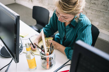 Hoher Winkel Blick auf selbstbewusste weibliche IT-Profi Schreiben auf Notizblock am Schreibtisch in kreativen Büro - MASF13296