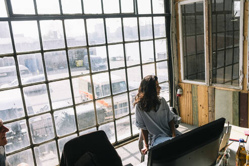 Junge Geschäftsfrau sitzt auf einem Stuhl vor dem Fenster im Sitzungssaal eines kreativen Arbeitsplatzes - MASF13304