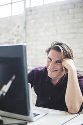 Portrait of smiling young male programmer coding at desk in office - MASF13318